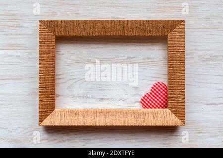 Wooden frame for photo, picture or text and handmade red checkered heart in corner on vintage wooden white painted wall background. Retro style Valent Stock Photo