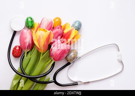 Stethoscope with colorful eggs and tulips on a white background. Stock Photo