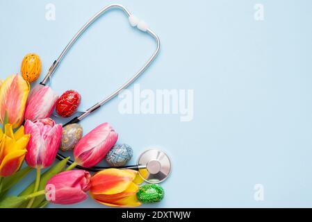 Stethoscope with colorful eggs and tulips on a blue background. copy space Stock Photo