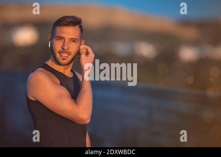 Young fit man listening music through wireless headphones during workout. Healthy lifestyle and technology Stock Photo