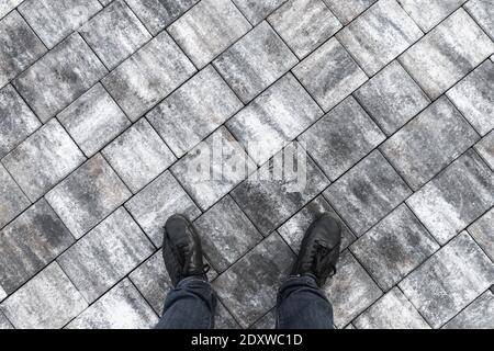 Male feet in jeans and black shoes standing on gray stone pavement, top view Stock Photo