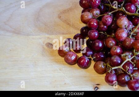 Looking down from above at a bunch of red grapes on a wooden chopping board. A shot with copy space which could be used as a background. Stock Photo