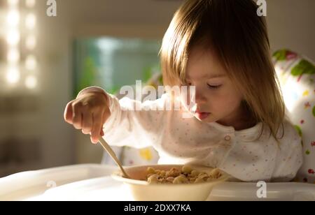 Small girl eats brakefast by herself with a spoon. Stock Photo