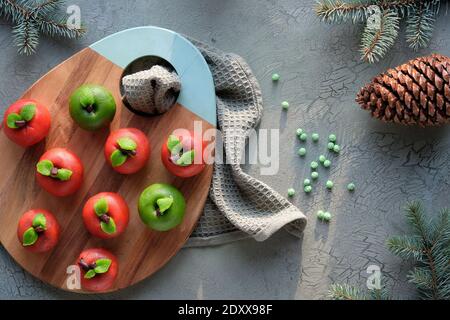 Marzipan sponge apples. Christmas dessert on wooden board. Winter decor, fir twigs and pine cone. Stock Photo