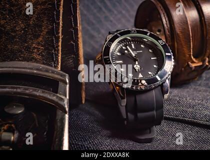 Close-up of a leather belt, a black and chrome watch and a leather bracelet on top of gray fabric Stock Photo
