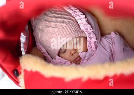 Cute baby in stroller on frosty winter day. Baby wearing woolen warm hat and mittens Stock Photo