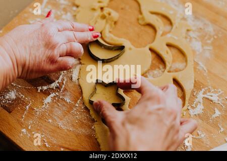 A closeup of women cutting the dough with shaped cookie cutters on a wooden surface Stock Photo