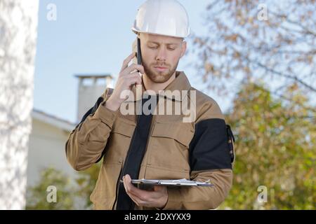 busy construction engineer talking on phone and holding clipboard Stock Photo