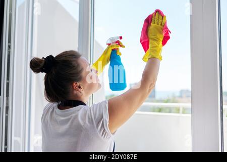 House cleaning, mature woman in rubber gloves wearing an apron washing windows Stock Photo