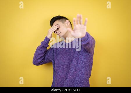 Young caucasian man over isolated yellow background covering eyes with hands and doing stop gesture with sad and fear expression. Embarrassed and nega Stock Photo