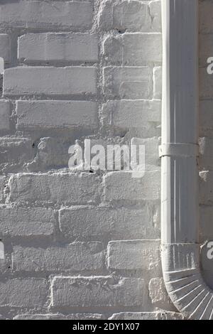 Vertical close-up of a white brick wall, a metal downspout at right, both painted white, all in bright side light. Stock Photo