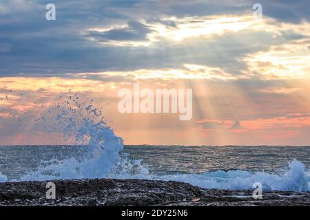Waves hitting the stones at the shore, background with dramatic purple, orange sky at sunset and sunbeams in Antalya Turkey, No people, selective focu Stock Photo