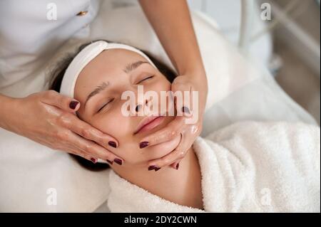 Cosmetologist making lifting facial massage for woman's face and neck. Stock Photo