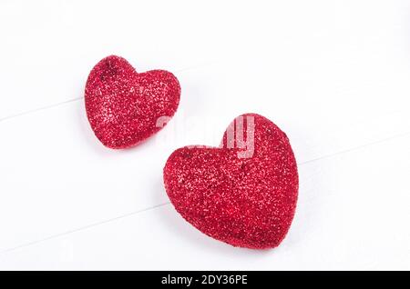 Two red glittering hearts on white wooden background. Stock Photo