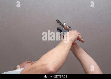 an adult man hangs a chandelier from the ceiling at home. Improvement and repair of premises. Stock Photo