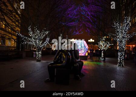 Two Men on a Bench (1995) bronze statue by Giles Penny in Canary Wharf, London, UK. Winter Lights festival, 2018. Stock Photo