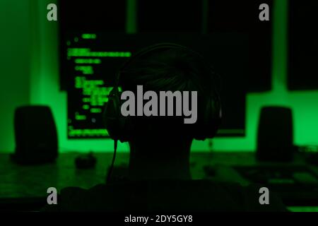 Hacker man looks at the screen. There are green texts on the black screen. Hacker writes code. People silhouette is looking at the screen. Stock Photo