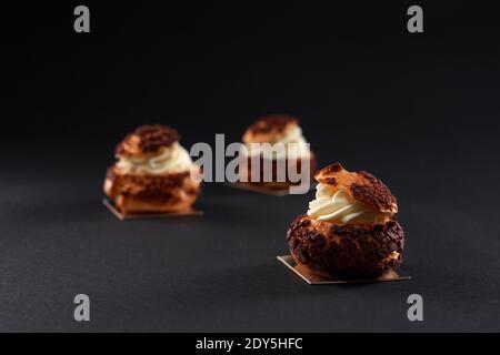 Three delicious fresh crunchy profiterole balls in row with sweet white creamy filling inside. Closeup of homemade tasty brown eclairs isolated on bla Stock Photo