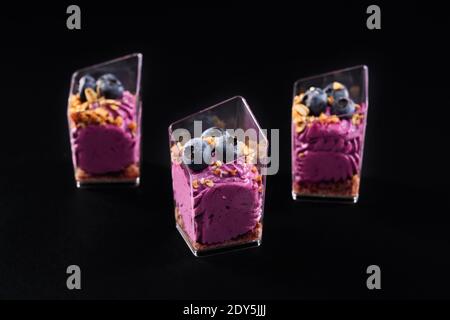 Closeup view of fresh homemade sweet dessert in three small glasses in row isolated on black background. Tasty parfait with granola, decorated with bl Stock Photo