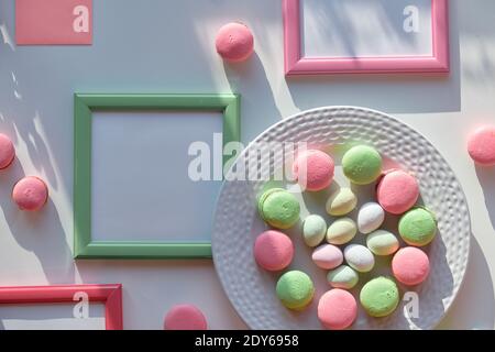 Easter sweets on white background with long shadows. Marzipan Easter eggs, pink and mint green macaroons on white plate. Text space in picture frames Stock Photo