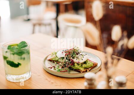Avocado toast, egg, microgreens on plate, glass of lemonade on table Stock Photo