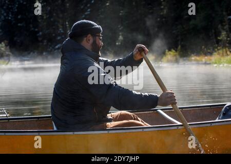 Close up of bearded man paddling canoe on a foggy lake in Canada Stock Photo