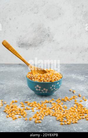 Raw corn kernels in blue bowl with wooden spoon Stock Photo
