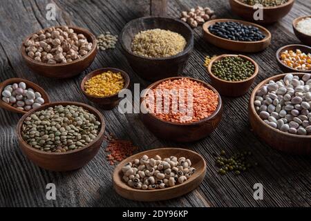Vegan protein source.Various assortment of legumes, lentils, chickpea and beans assortment in different bowls on wooden table. Top view. Stock Photo
