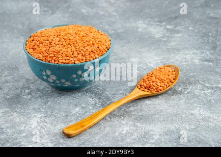 Red lentils in blue bowl with wooden spoon on marble surface Stock Photo