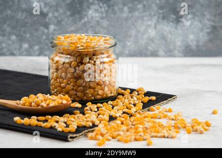 Glass jar of corn kernels with spoon on black cutting board Stock Photo