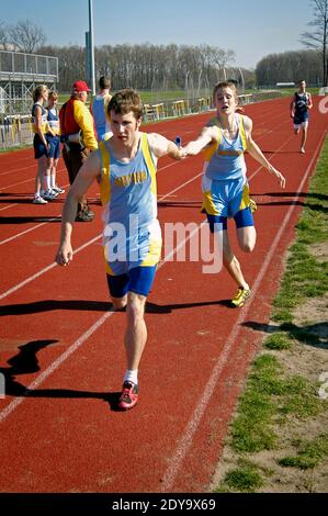 High School track and field event paticipant in the baton pass in a running relay eveny Stock Photo