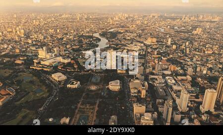 Designed park at high skyscrapers on town streets. Sun shine over cityscape with plants, trees. Philippines capital city of Manila. Cinematic sunlight at modern urban buildings aerial view Stock Photo