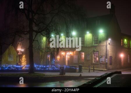 Christmas tree and lights in the fog outside the old manse hotel at night. Bourton on the Water, Cotswolds, Gloucestershire, England Stock Photo