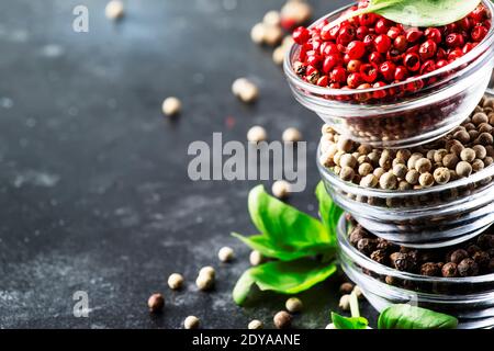 Black, white and pink rose peppers in bowls, assorted spices on gray kitchen table, selective focus Stock Photo