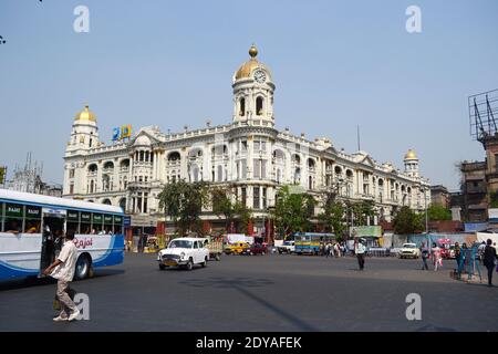 Kolkata, India - March, 2014: Vehicles and people on crossroad in front of Metropolitan Building in Esplanade. Historical house with clock tower in hi Stock Photo