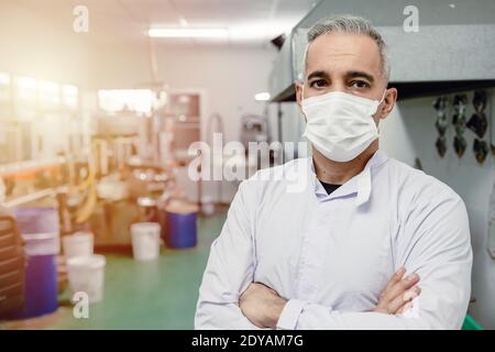 Confidence european high skilled worker middle age 40-50 standing portrait in factory with face mask. Stock Photo