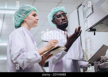 Woman production supervisor working with African worker in food factory to checking and report machine problem to engineer in production line. Stock Photo