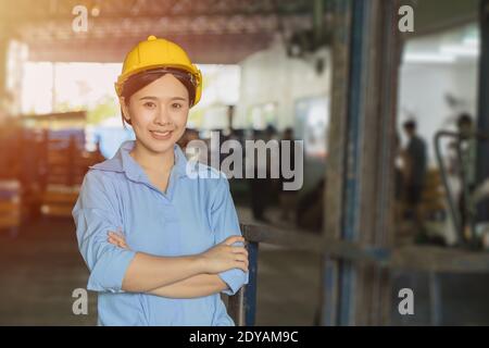 Young Asian smart woman working as foreman head engineer manager at logistic warehouse portrait smiling arms crossed. Stock Photo