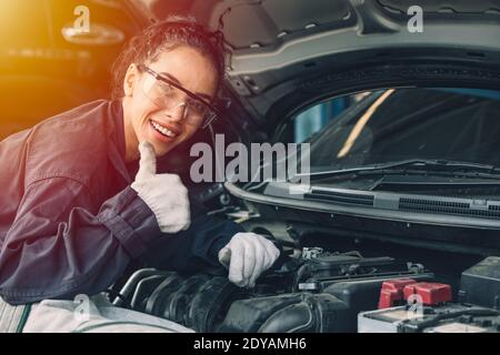 Portrait happy working woman work for auto mechanic job in garage hand thumbs up sign for good condition car engine Stock Photo