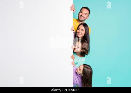 Photo portrait of big family hiding behind big white placard poster with small children isolated on vivid teal colored background Stock Photo