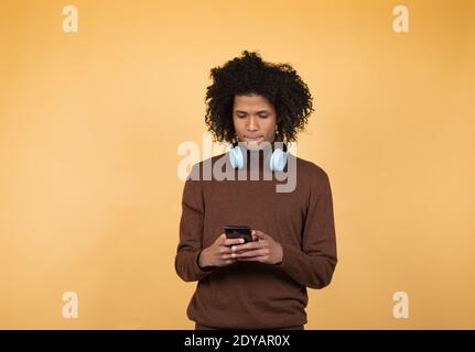 A shot of a happy young afro man in headphones  looking at his phone - social connection Stock Photo