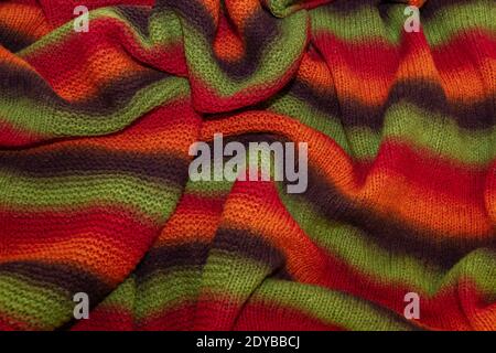 Large handmade merino wool blanket, super chunky yarn, fashion concept. Close-up of a knitted designer blanket in red, green and brown wool. Selective Stock Photo