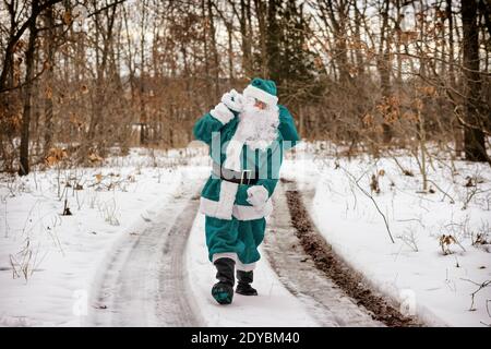 Christmas Elf in green suit dress brings walking through the winter forest carrying New Year's Christmas presents on and looking away
