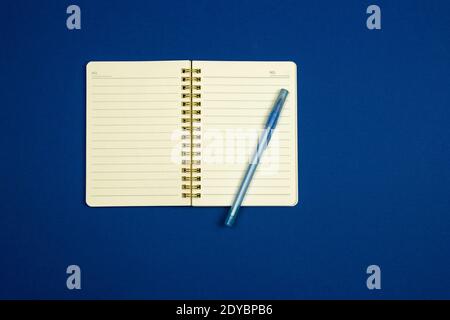Notepad for notes and pen on a simple blue background, flat design, top view, copy space, workplace photo Stock Photo