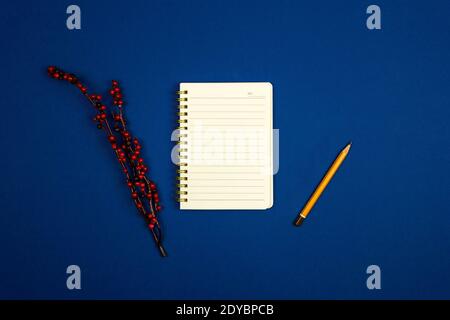 Conceptual workplace with notepad and pencil, branch and decorations on blue background, top view, copy space photo Stock Photo