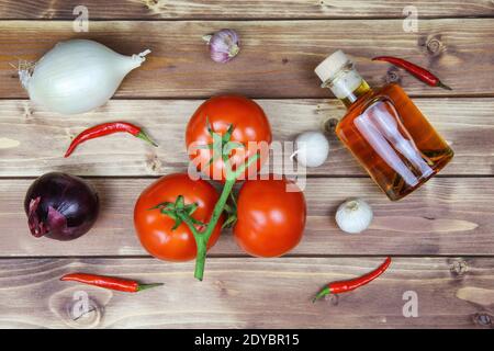 Top down view on raw uncooked isolated white and red onions, tomatoes vine, bottle olive oil and chillies. Brown natural rustic wooden background. Hea Stock Photo