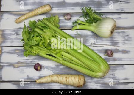 Top down view on raw uncooked isolated celery stalk, garlic and fennel bulbs, parsley roots. White natural rustic wooden background. Healthy ingredien Stock Photo