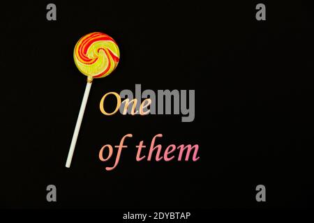 One of them, slogan on a black background with lollipop, copy space photo Stock Photo