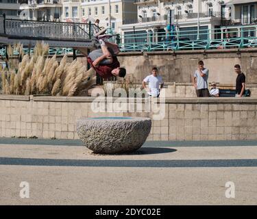 Young man doing Parkour jumps on the Brighton beach esplanade, caught in mid air doing summersault Stock Photo