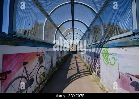 Fenced covered pedestrian walkway going over train tracks in Lewes, England, on sunny day, with shadow shapes from the links Stock Photo